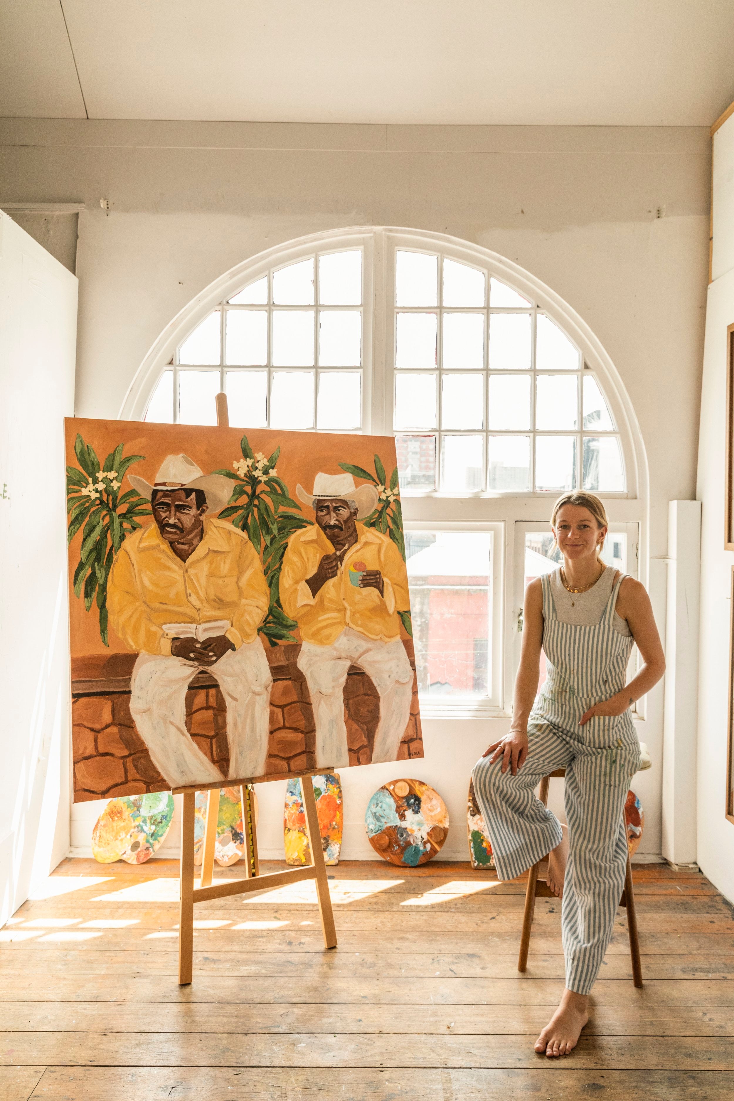 Artist Sammy Veall Sitting on a stool next to one of her Original Paintings